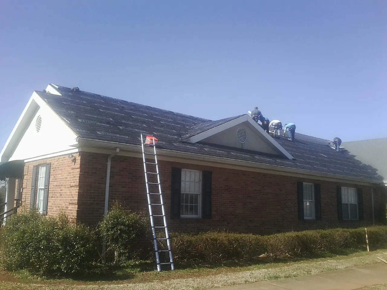 Crew tearing shingles off a brick ranch roof with a ladder set — Metal Roof Repair work by our crew in Lacrosse