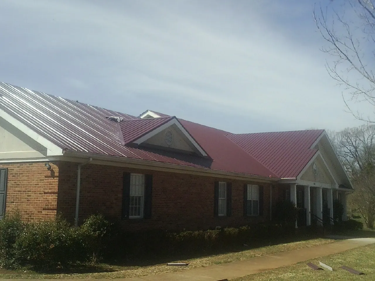 Red metal roof with gabled entries on a long brick building, from a Hail Damage Roof Repair job in Lacrosse