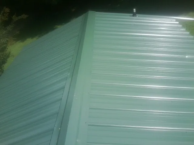 New green metal panels meeting at the ridge of a roof — Flat Roof Repair work by our crew in Lacrosse