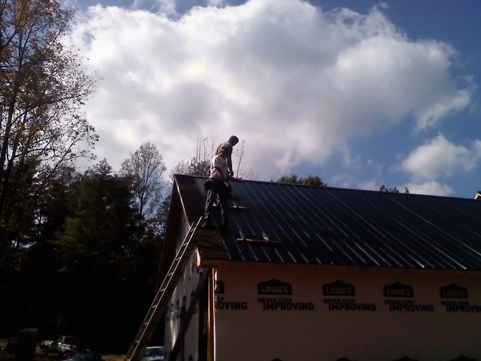 Roofer fastening dark metal panels high against a cloudy sky, from a Roof Inspection job in Lacrosse