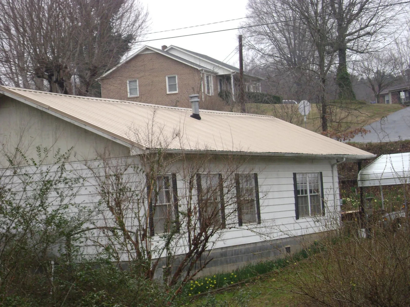 Tan metal roof on a white sided house set into a hillside — Commercial Roofing by Roofing Brothers in Lacrosse